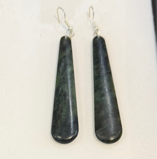 A pair of teardrop-shaped dark green and black stone drop earrings with silver fishhook wires, displayed on a white textured surface.