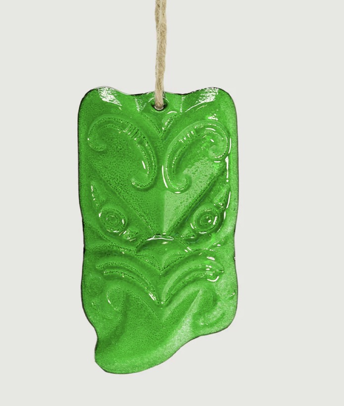 Green glass Maori wheku wall hanging ornament with intricate patterns on a white background