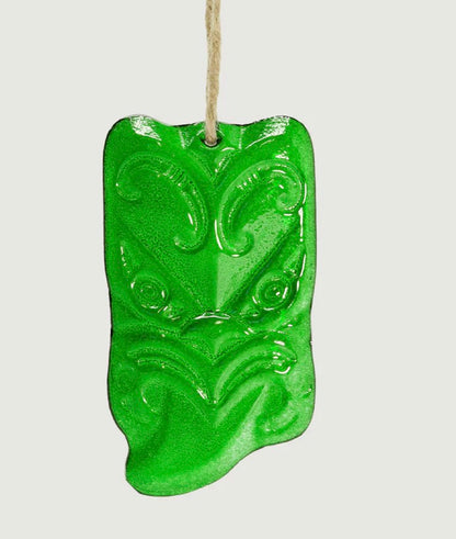 Green glass Maori wheku wall hanging ornament with intricate patterns on a white background