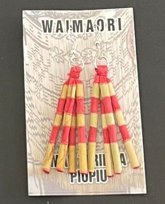 Red and yellow striped piupiu earrings on a Wai-Maori branded card against a dark background