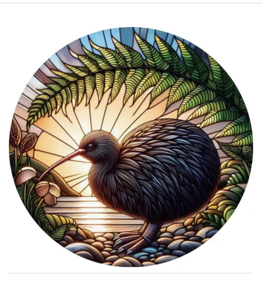 A circular stained-glass-style artwork showing a kiwi bird standing among rocks and fern leaves, with a glowing sunburst behind it, isolated on a white background.