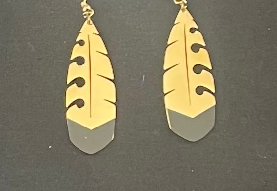 Gold and silver feather-shaped earrings on a dark background