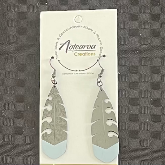 Feather-shaped maori earrings on a branded card against a textured gray background