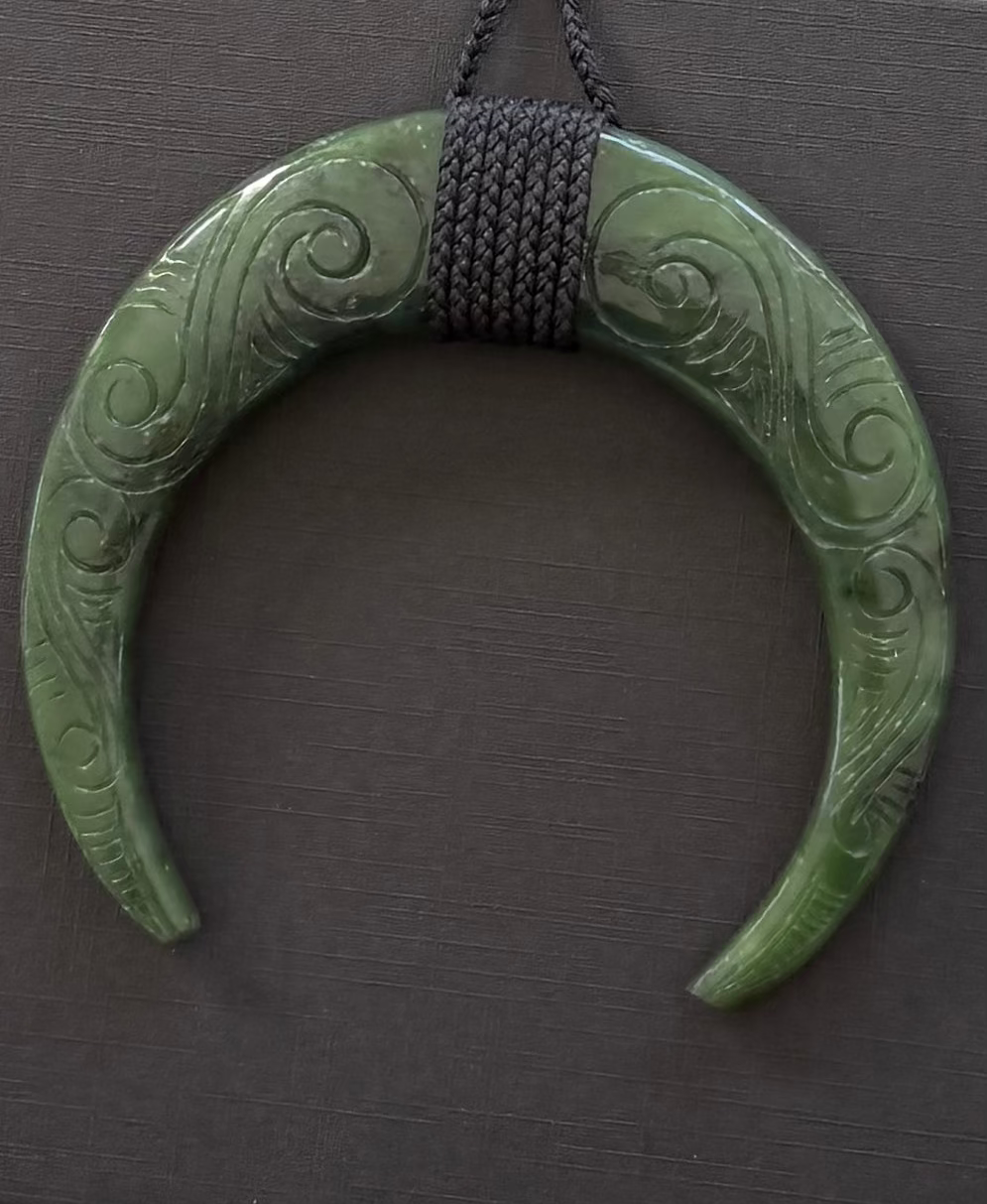 Greenstone pig tusk jade necklace with intricate carvings on a dark background