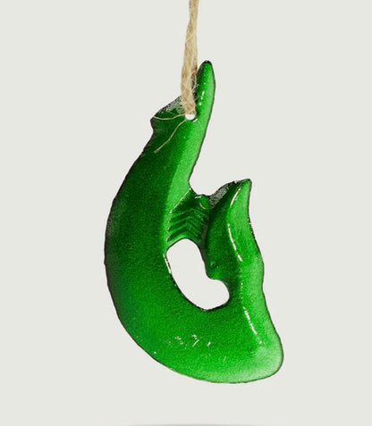 Green glass Maori fish hook hanging on a white background