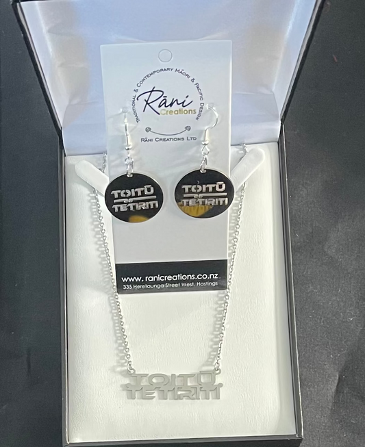 Silver necklace and earrings with 'Tortu Tetru' design in a Rani Creations packaging on a dark background.