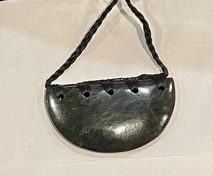 Greenstone pendant with holes on a string against a beige background
