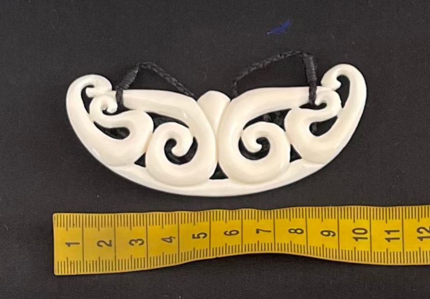 White spiral decorative bone carving necklace on a black background with a yellow measuring tape for scale.