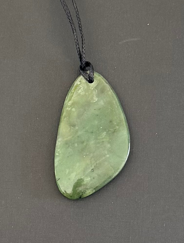 Greenstone pendant on a black cord against a gray background