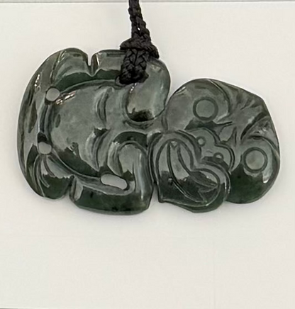 Greenstone tiki jade pendant with intricate carvings on a white background