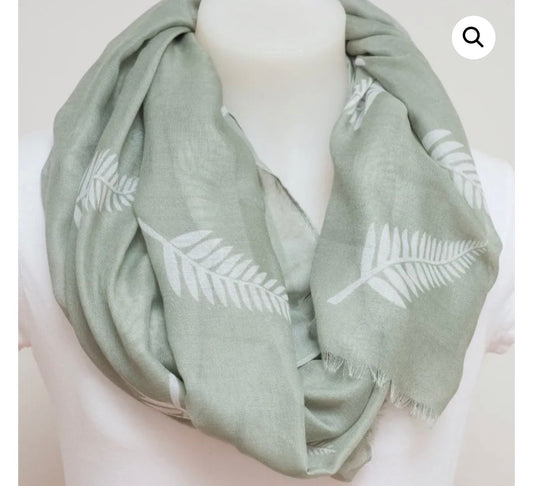 A sage green infinity scarf with a white fern leaf pattern, draped on a white mannequin torso.