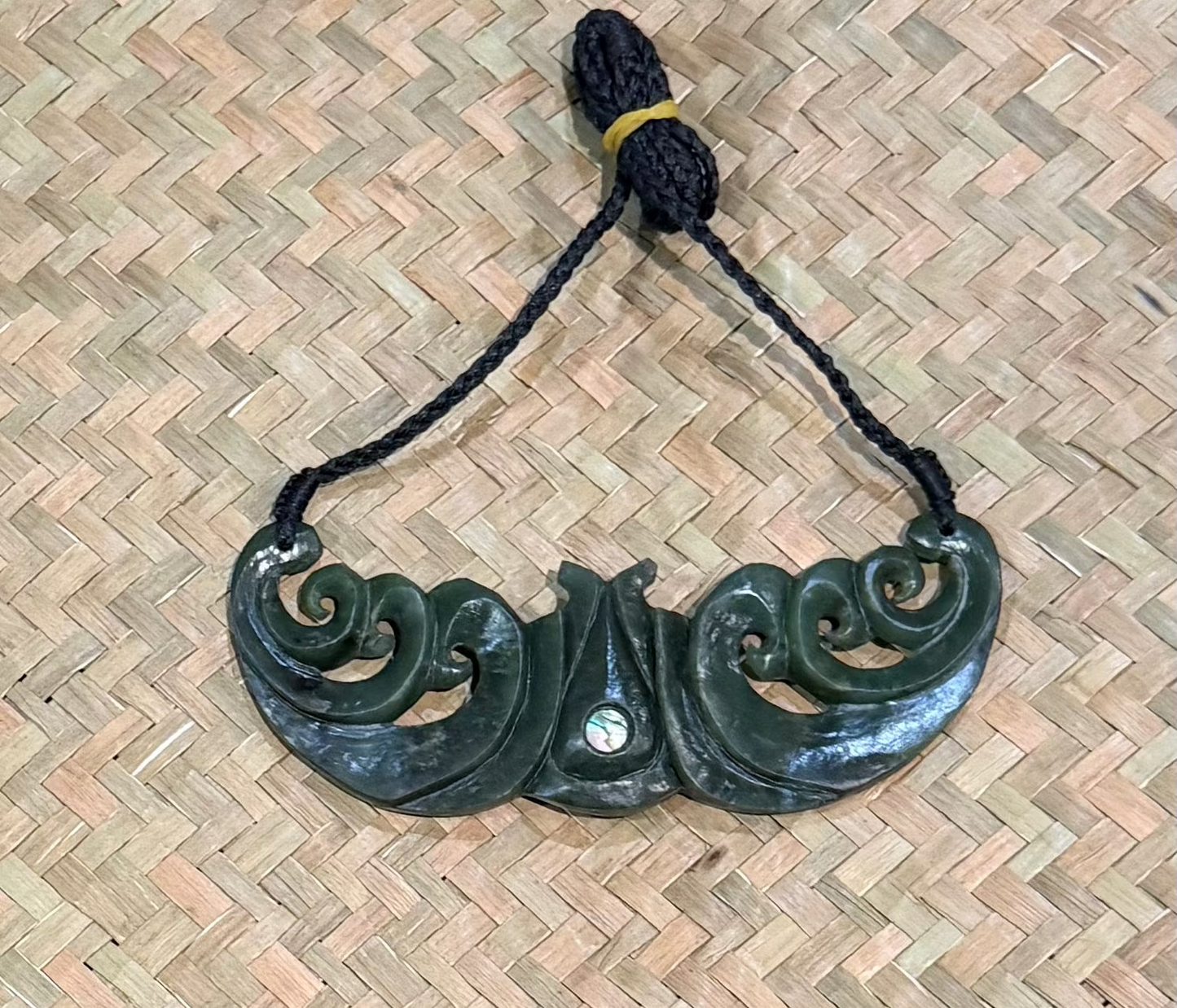 Greenstone pounamu jade necklace with black cord on a woven mat background
