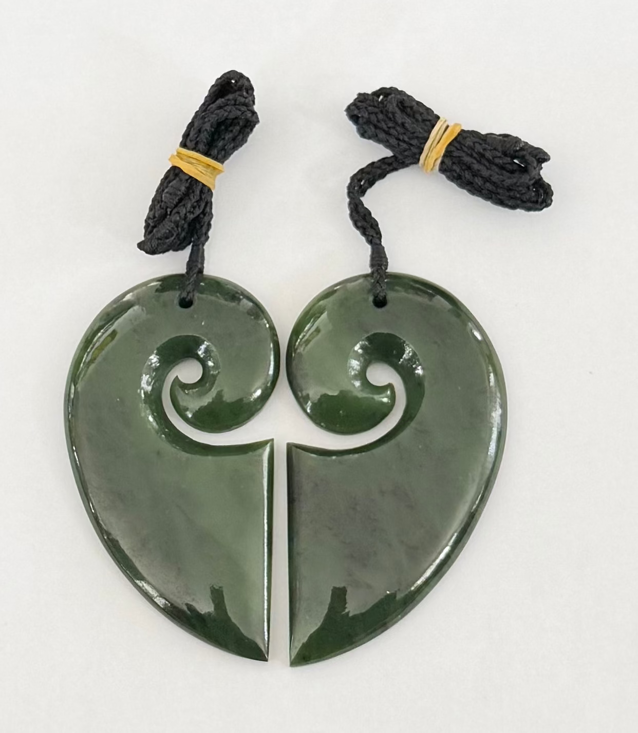 Two greenstone jade pendants on black cord against a white background