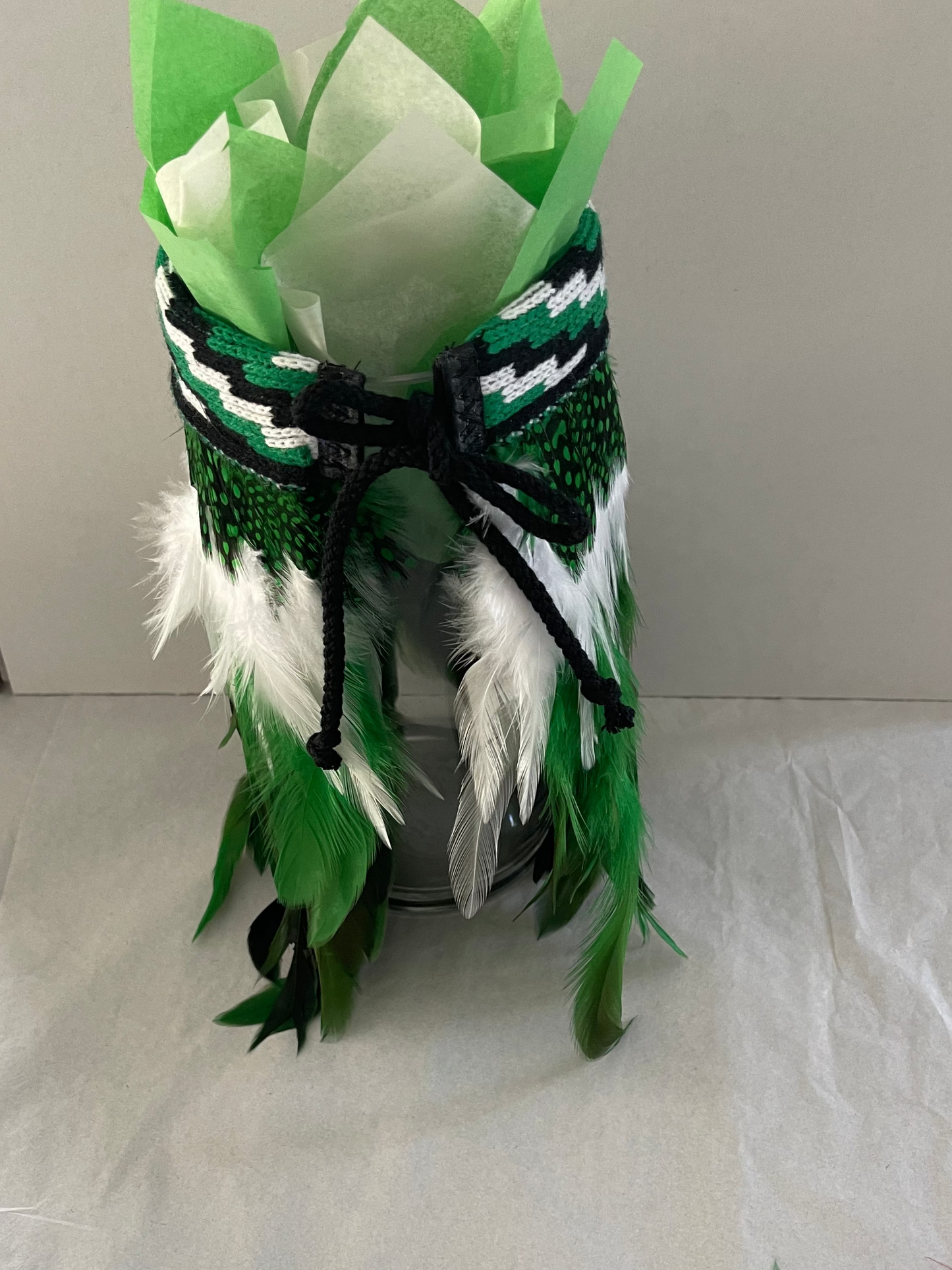Decorative item with green feathers and ribbons on a white surface